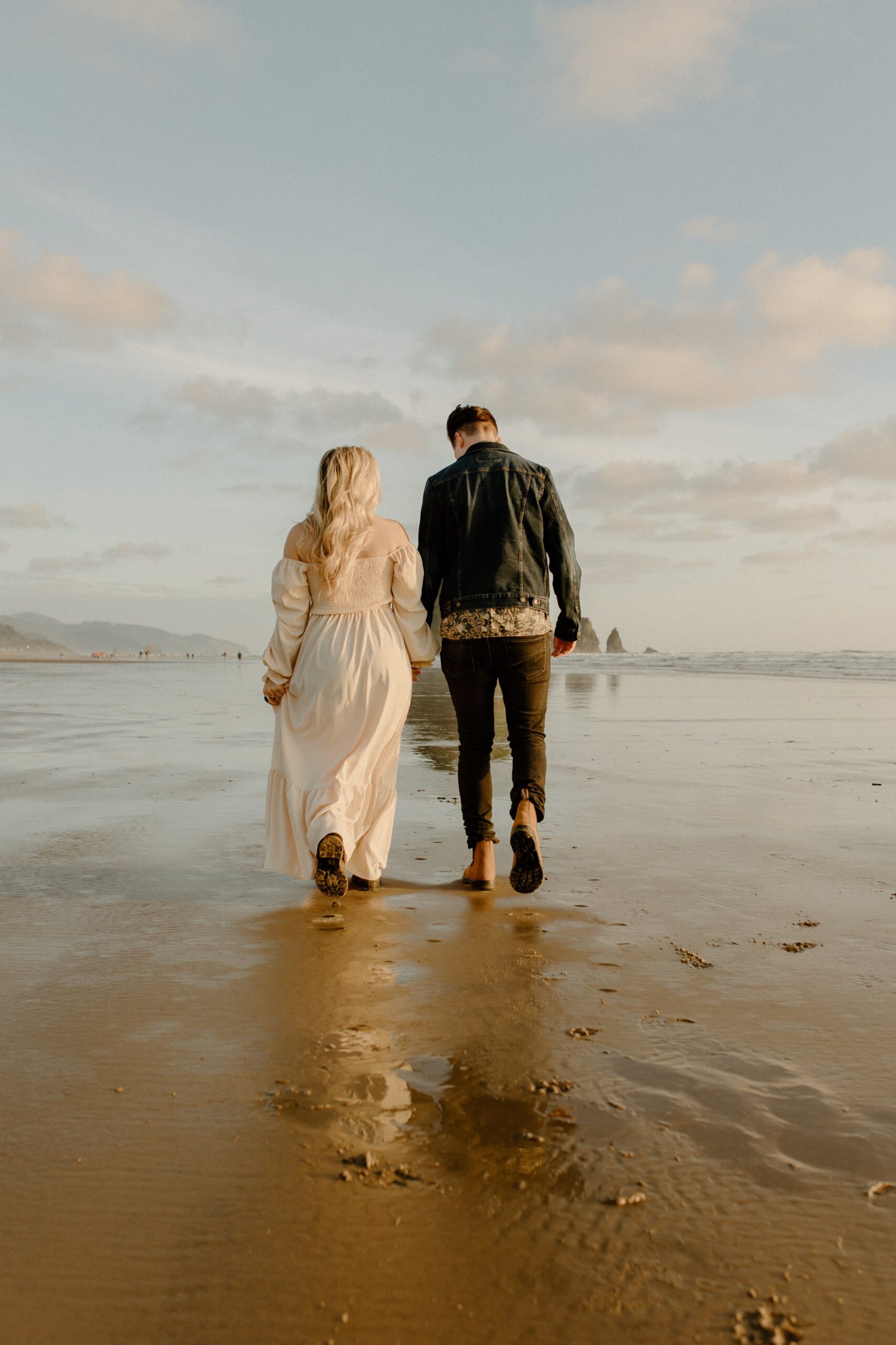 man and woman holding hands while walking on sand at beach, film couple photographer
