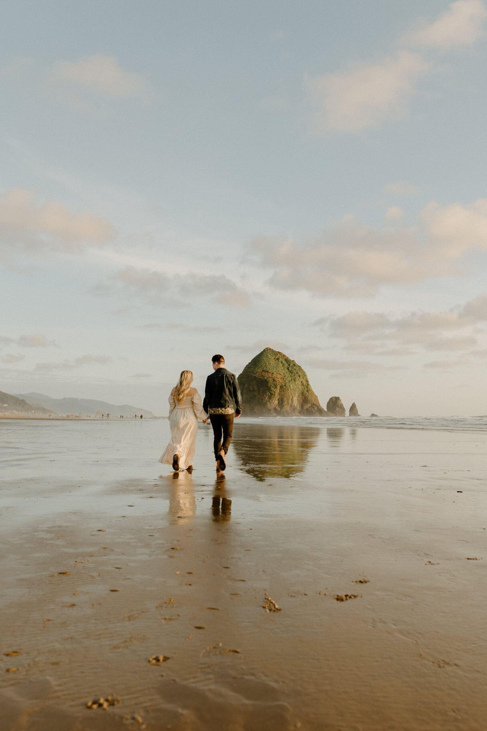 woman and man holding hands while walking on sand at beach in Oregon