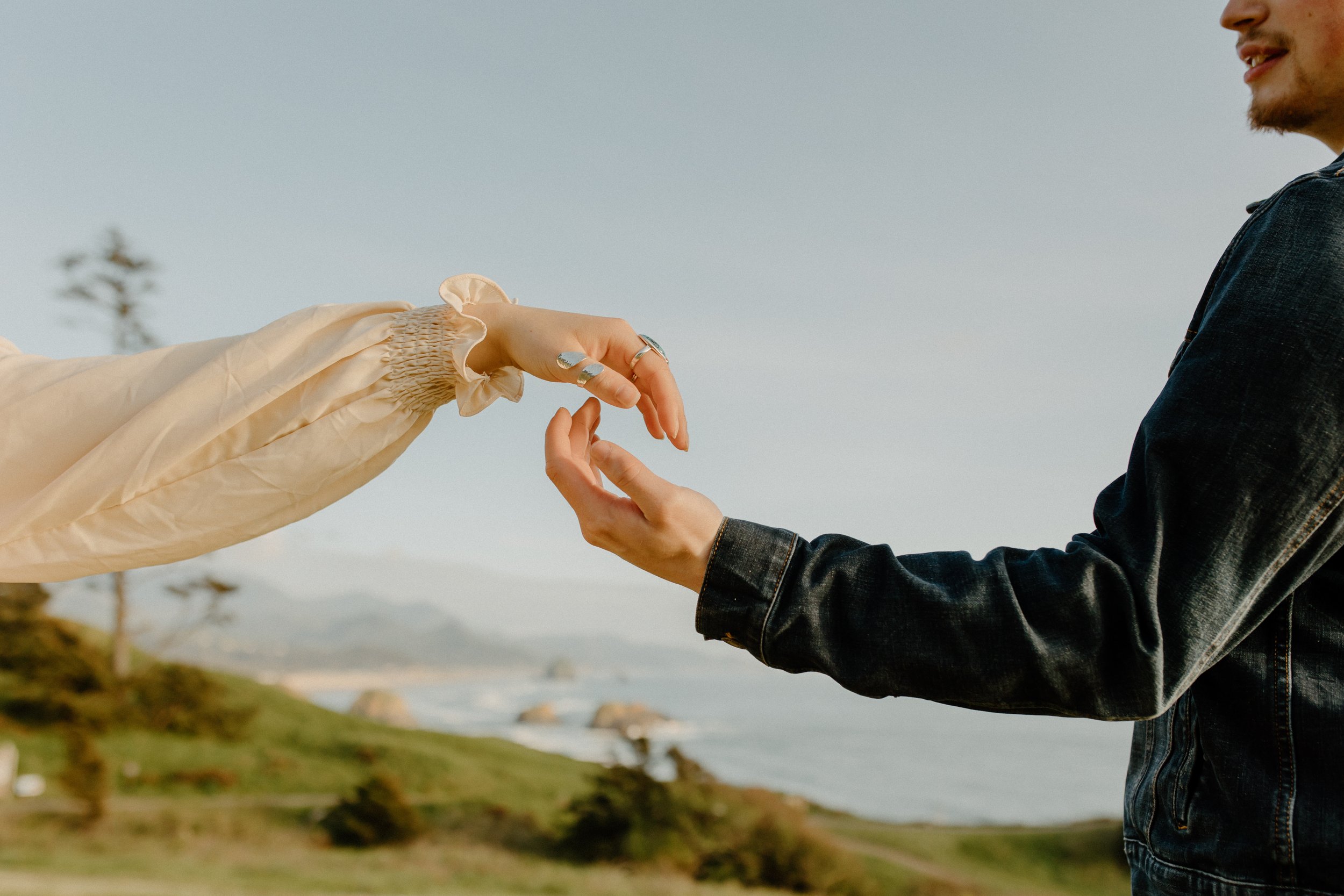 man and woman hovering hands over each other with background of ocean and meadow on the oregon coast