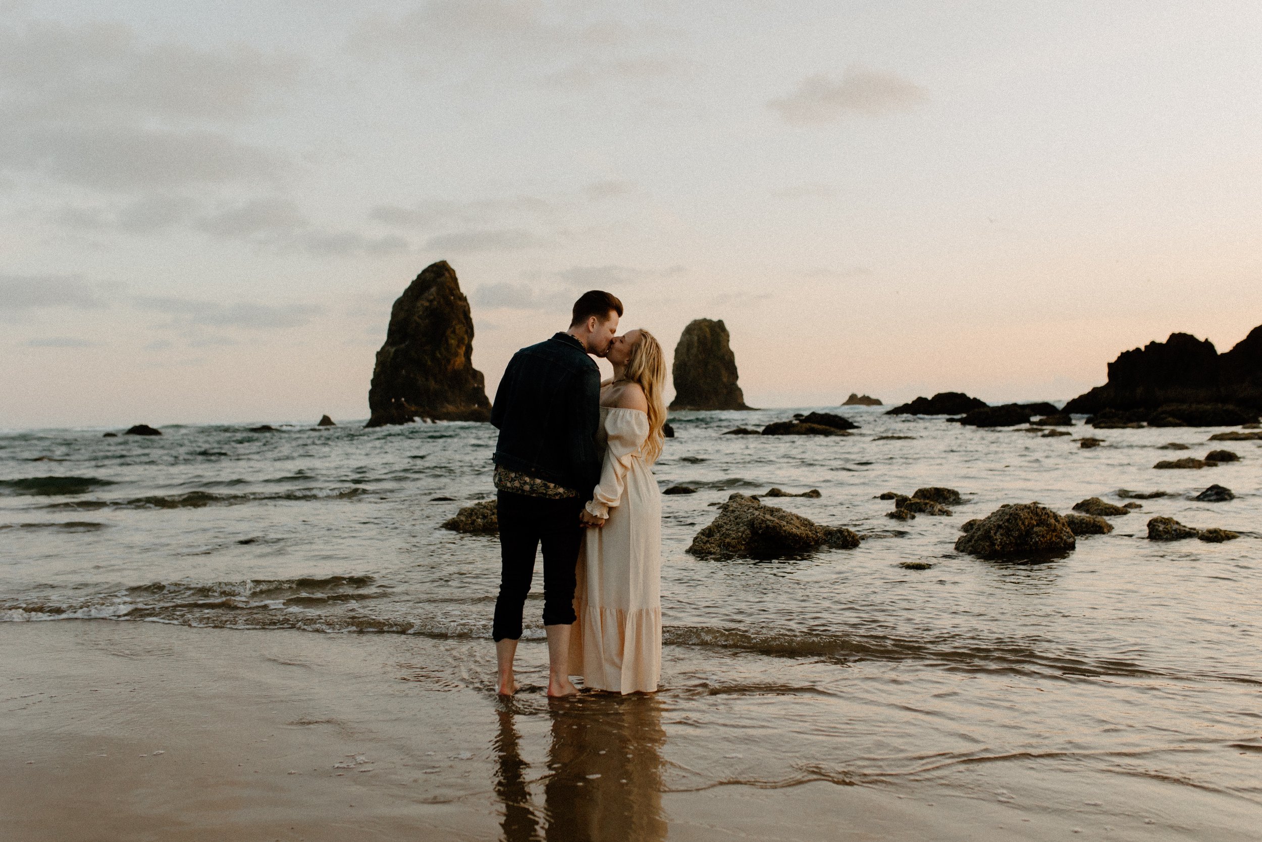 man kissing woman at beach in front of rocks at Oregon beach, destination couples photogapher