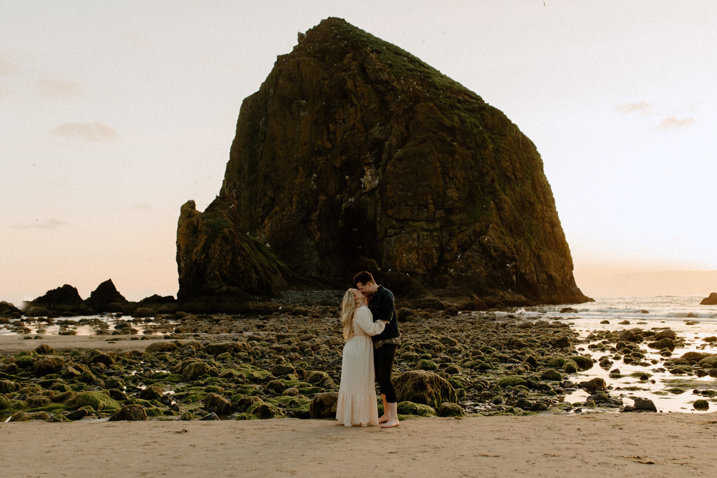 woman and man kissing holding each other while standing in front of moss covered rocks in ocean in Oregon, Oregon wedding photographers
