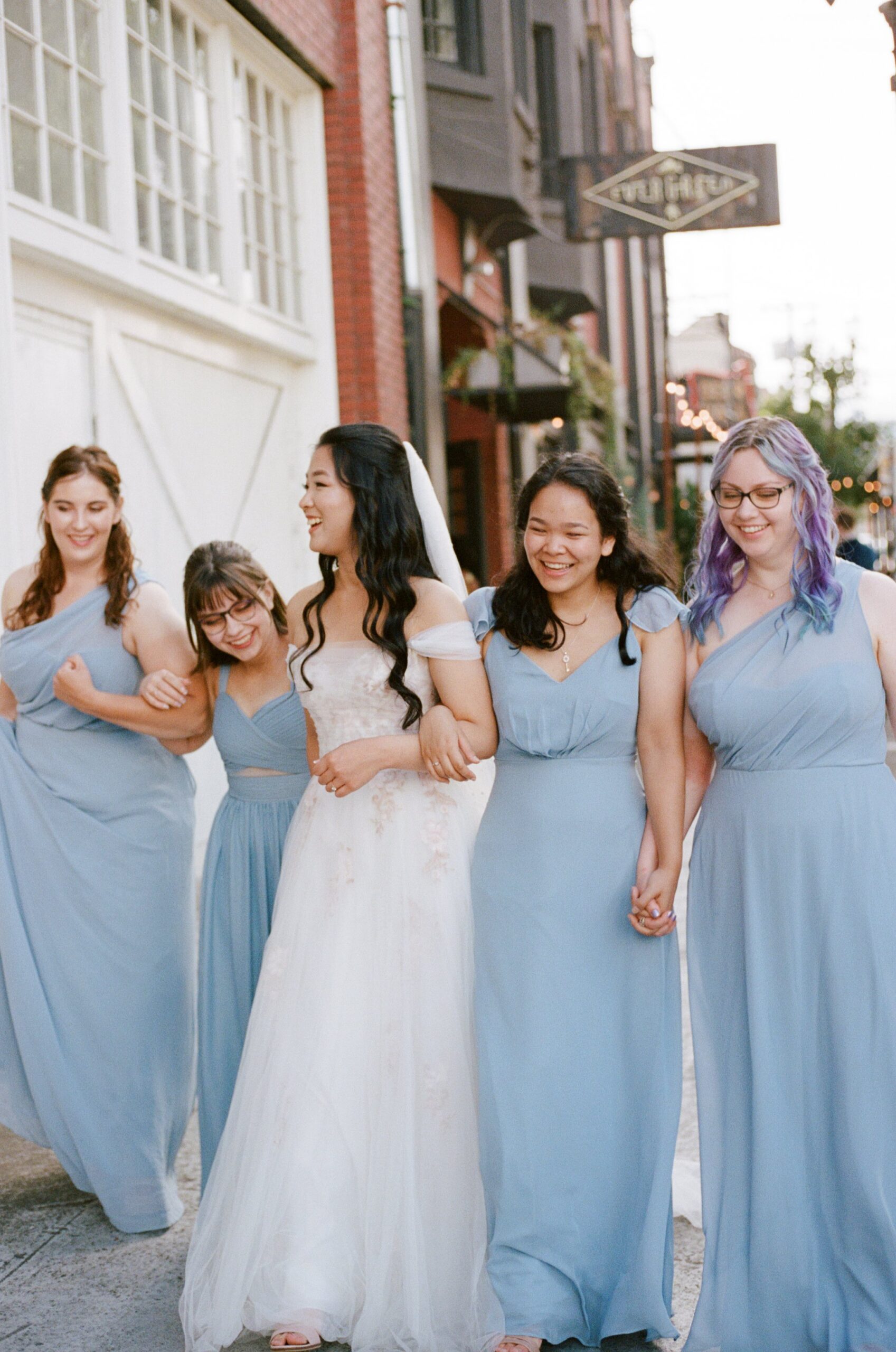 bride and bridesmaids holding hands and laughing while walking to wedding ceremony. Film photographer in Oregon