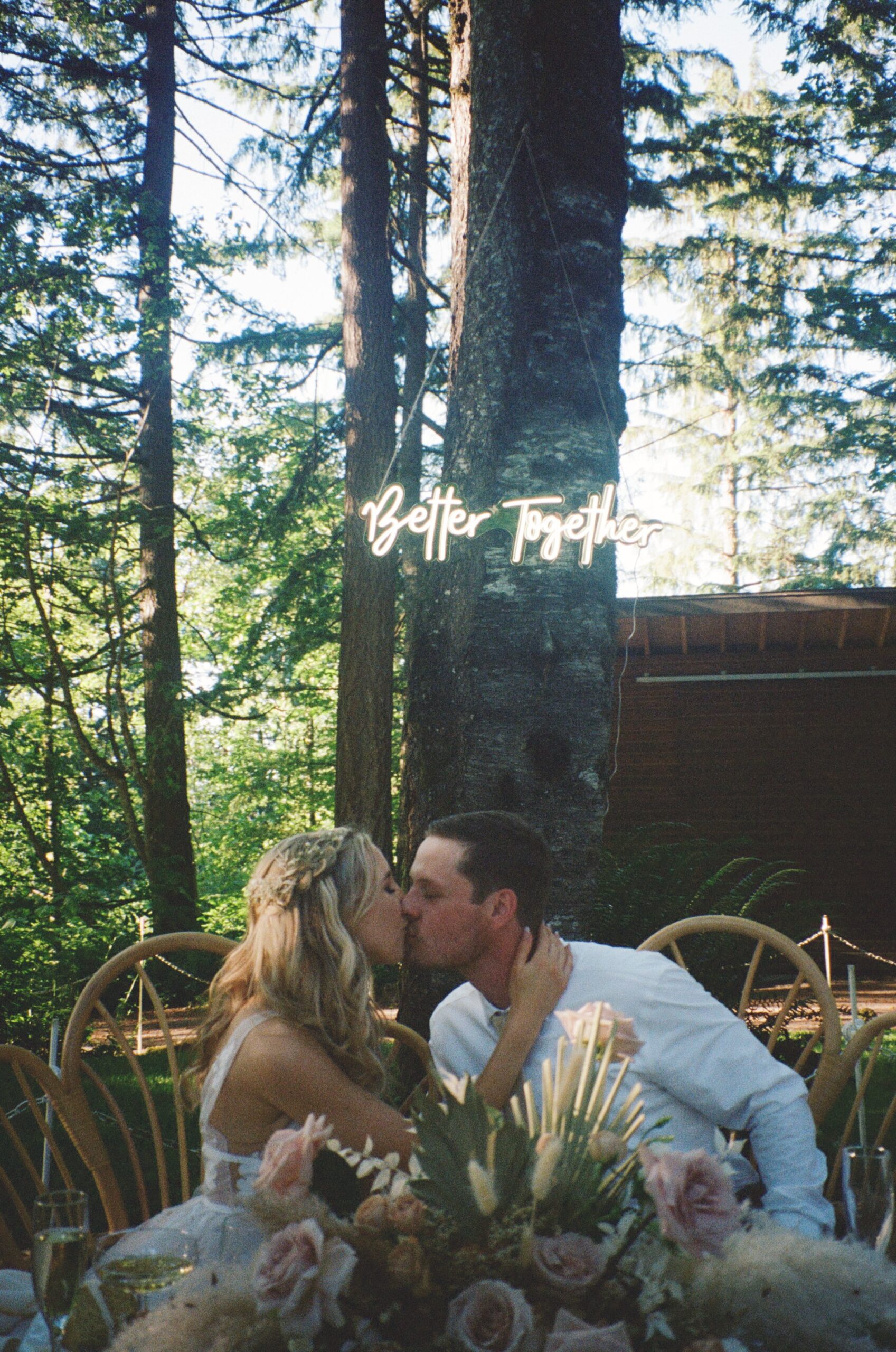 Bride and groom kissing at wedding table with better together sign in background. Oregon Wedding photographer, film photography