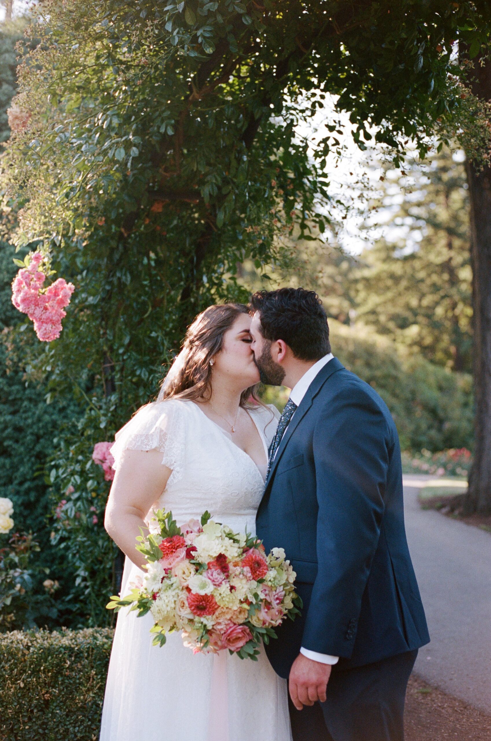 bride and groom kissing under arch with pink flowers. film photography in oregon for weddings