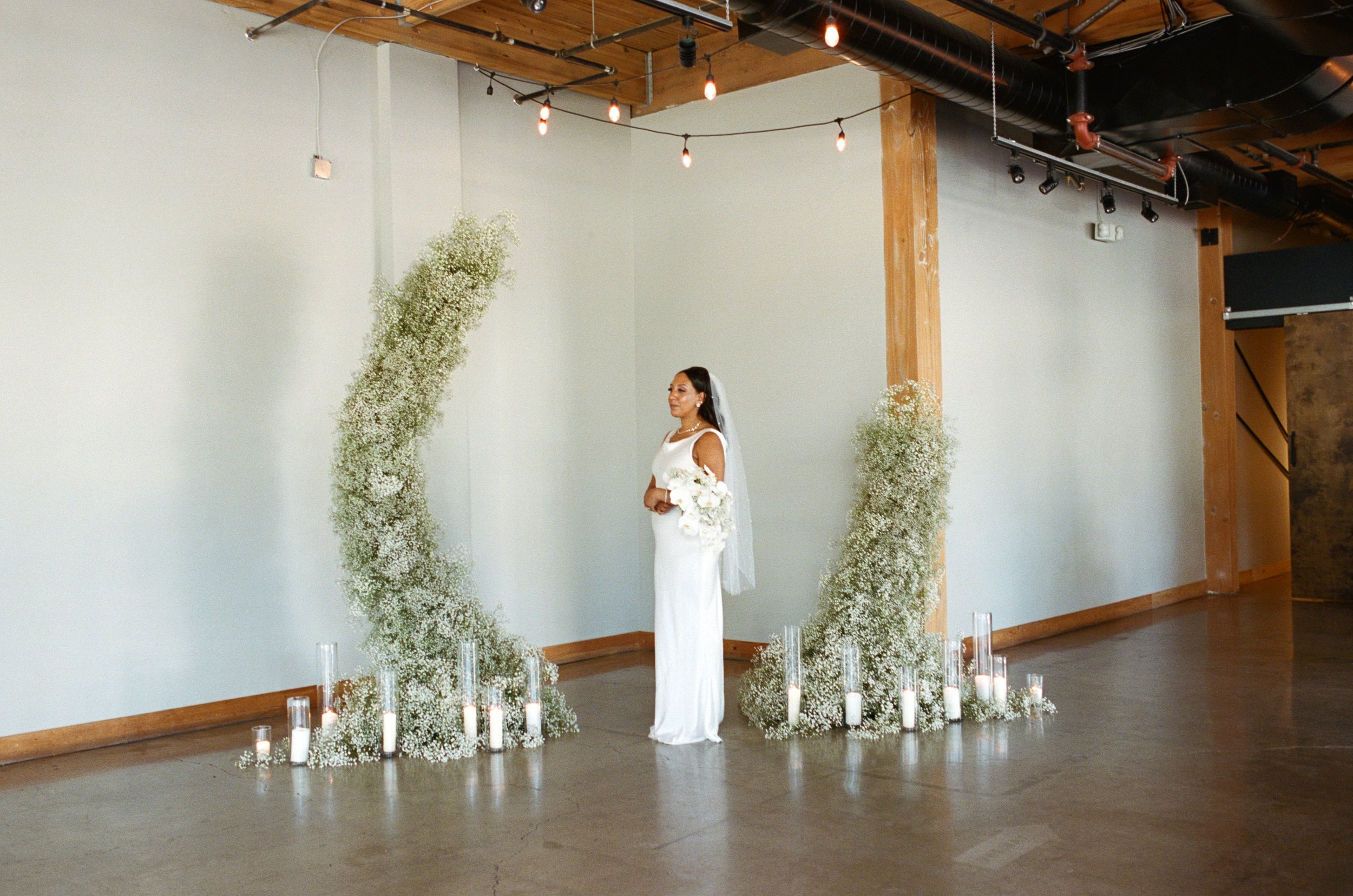 woman holding flower bouquet standing in between flower arch for wedding photos. Oregon wedding film photographers