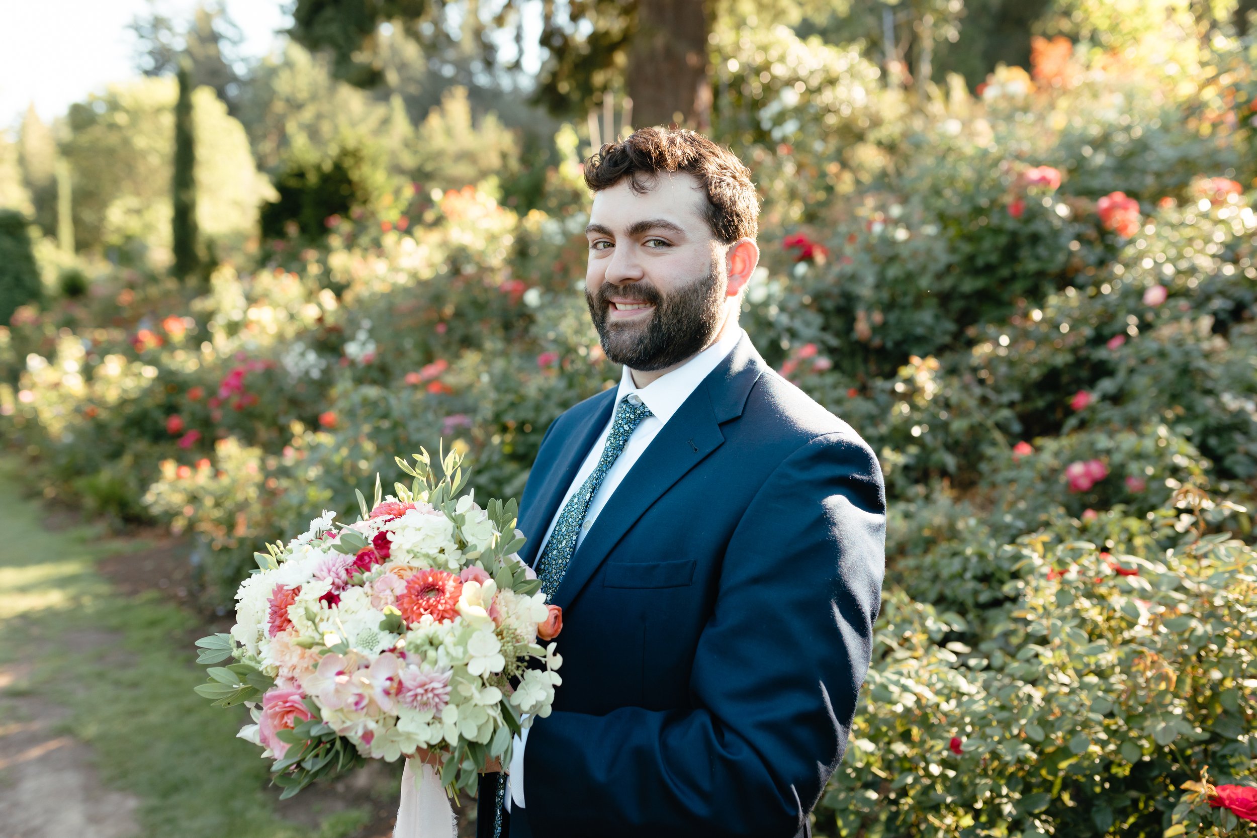  groom holding elopement bouquet at portland international rose garden in blue suit 